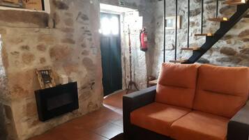 Una sala de estar acogedora con una pared de piedra, una chimenea, un sofá y una escalera.