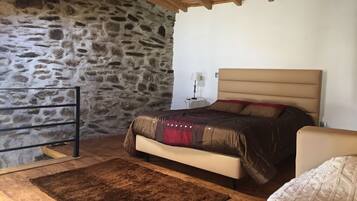 Une chambre avec un mur en pierre, un lit avec une tête de lit, une table de chevet, une lampe et un plancher en bois.