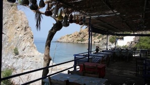 En restaurant ved vandet med udendørs siddepladser, med udsigt over en klippefyldt kystlinje og havet.