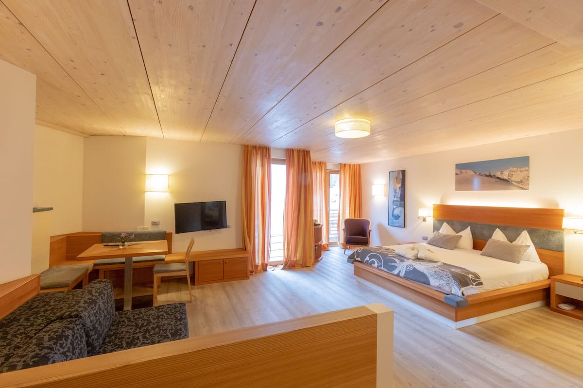 Habitación de hotel con techo de madera, una cama con cabecera, un escritorio con silla, un sofá y un televisor.