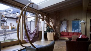 Ein großzügiger Wohnbereich mit einem großen Fenster, einem Hängesessel, einem roten Sofa und einem Korbstuhl.