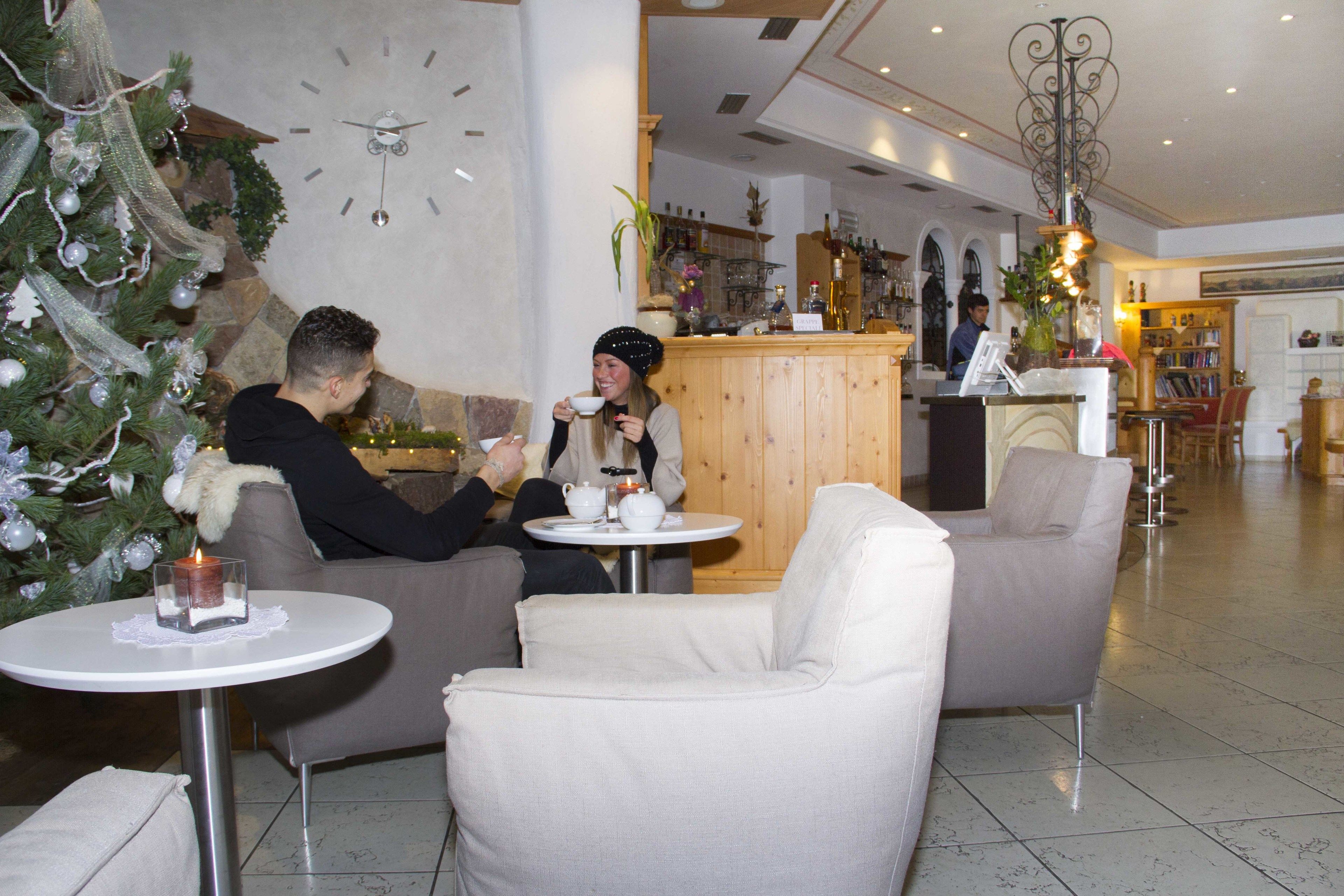 Ambiente acolhedor em ambiente interno, com árvore de Natal, relógio na parede e um espaço de bar ao fundo.