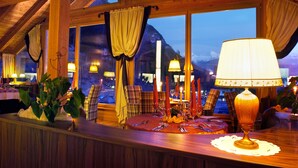 Ein Restaurant mit Holzvertäfelung, großen Fenstern und einem für das Essen gedeckten Tisch mit Kerzen und einer Lampe.