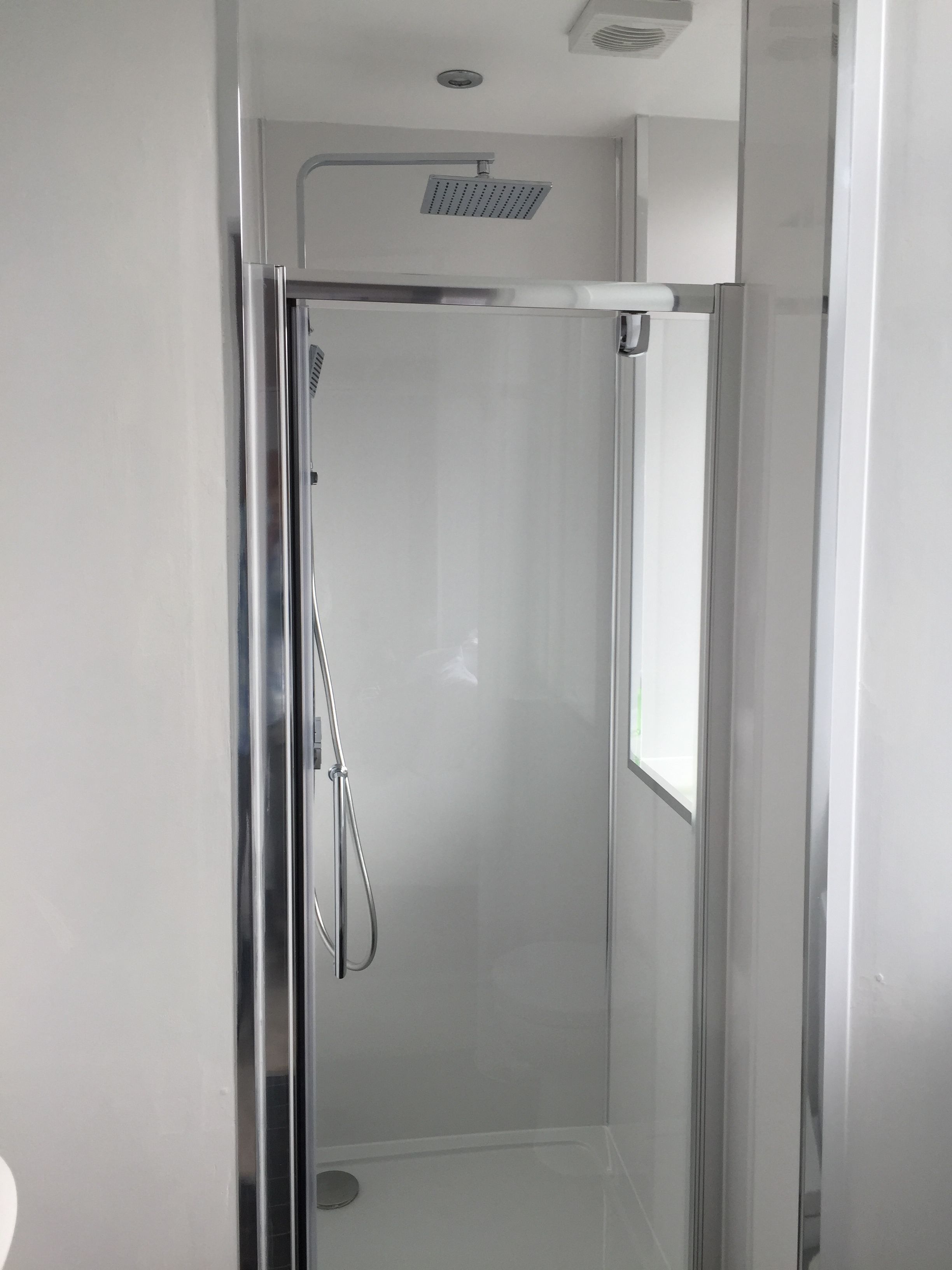Une cabine de douche moderne et épurée, entièrement vitrée, dotée d’un pommeau de douche à main et d’une douchette à pluie fixée au plafond.