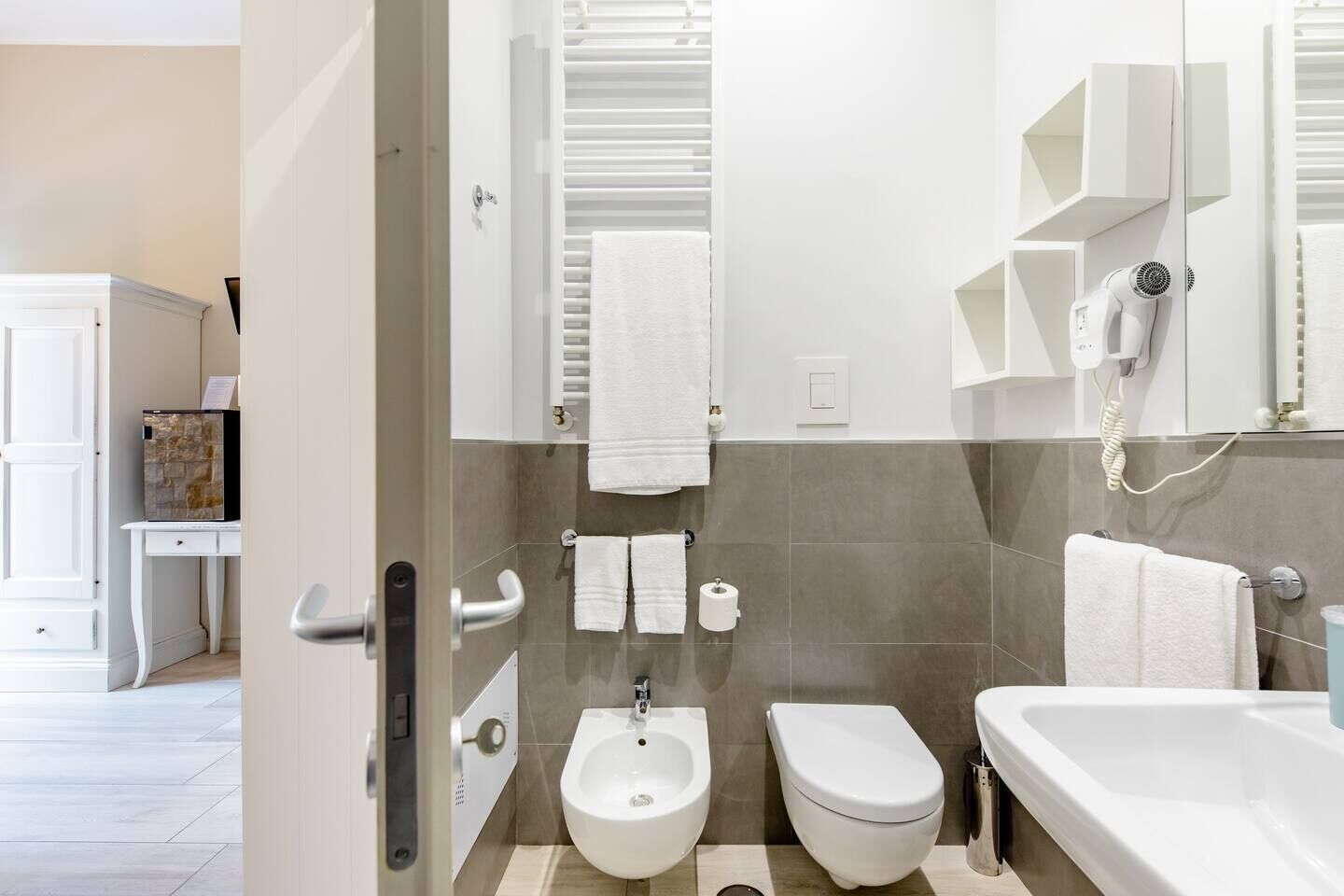 Un baño moderno con bidé, inodoro y bañera. Hay toallas blancas y un secador de pelo en la pared.