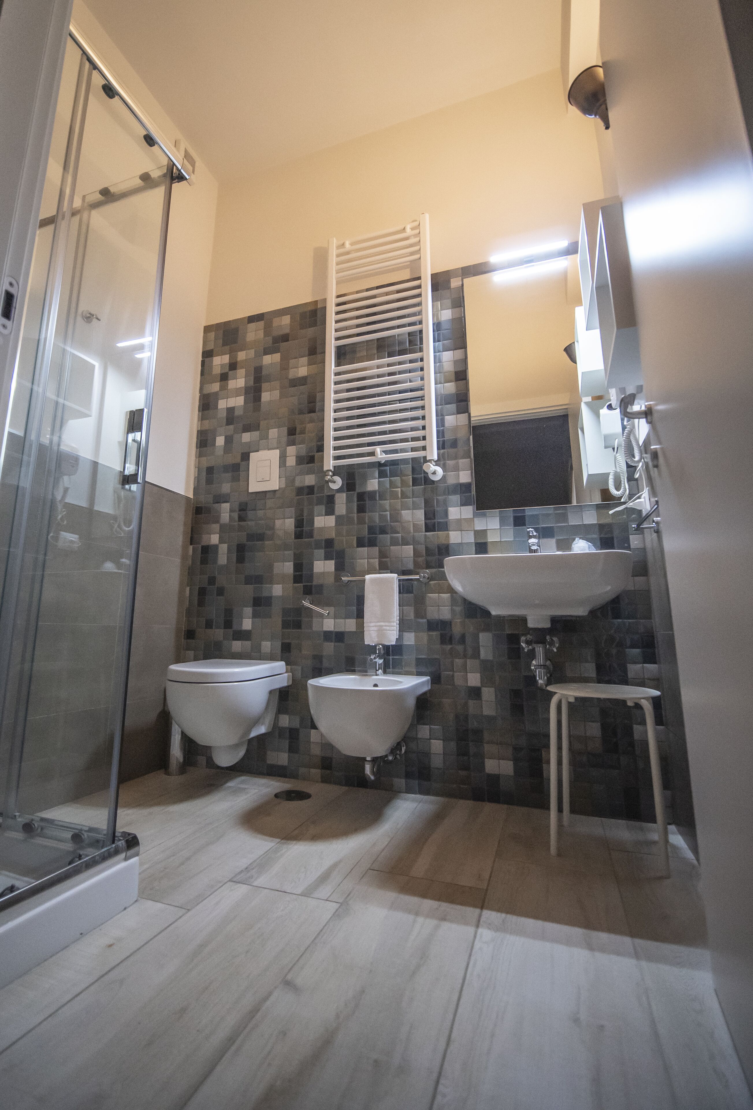 A bathroom with a glass shower enclosure, two toilets, a sink, and a tiled backsplash.