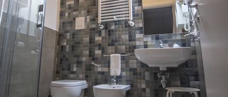 A bathroom with a glass shower enclosure, two toilets, a sink, and a tiled backsplash.