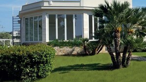 Un edificio moderno de una sola planta con fachada de vidrio curvo, rodeado de abundante vegetación y palmeras.