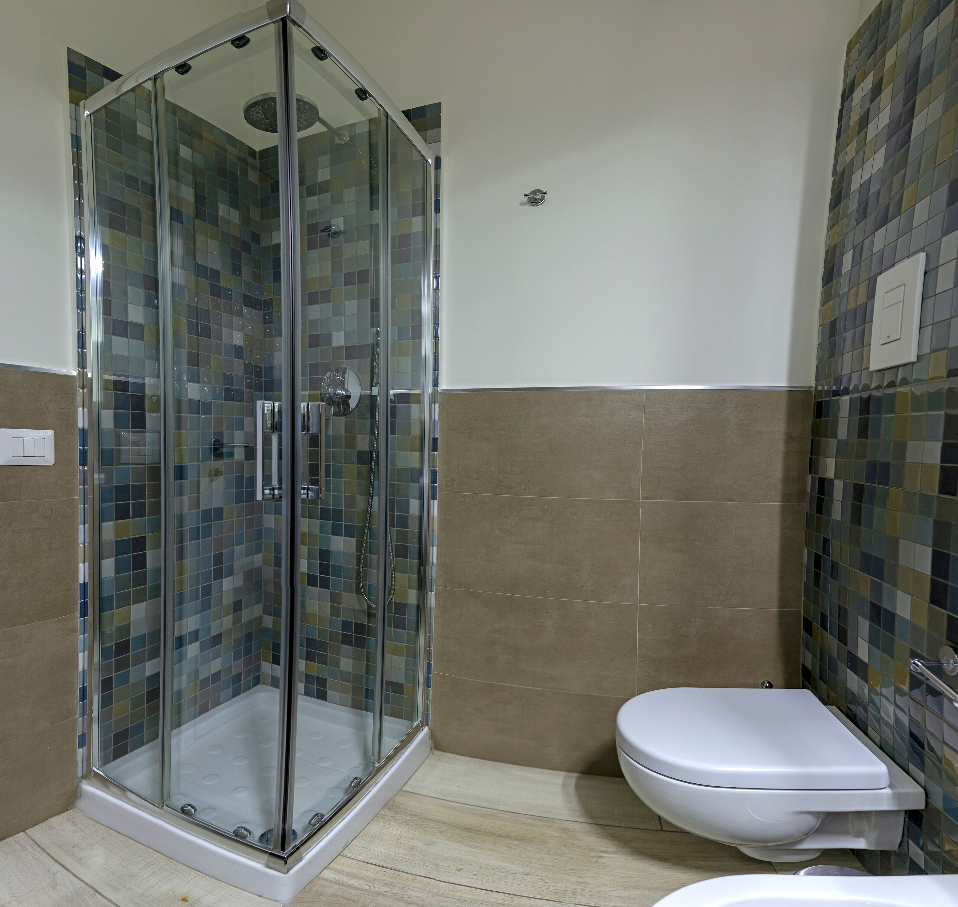 A shower enclosure with a glass door, a toilet, and tiled walls.