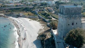 A coastal area with a beach, a stone tower, and residential buildings in the background.
