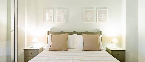 A hotel room with a large bed, two bedside tables, a nightstand, and a glass door.