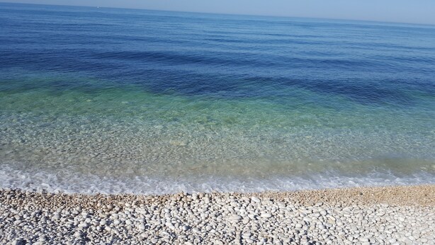 Una playa de adoquines con agua cristalina y un barco a lo lejos.