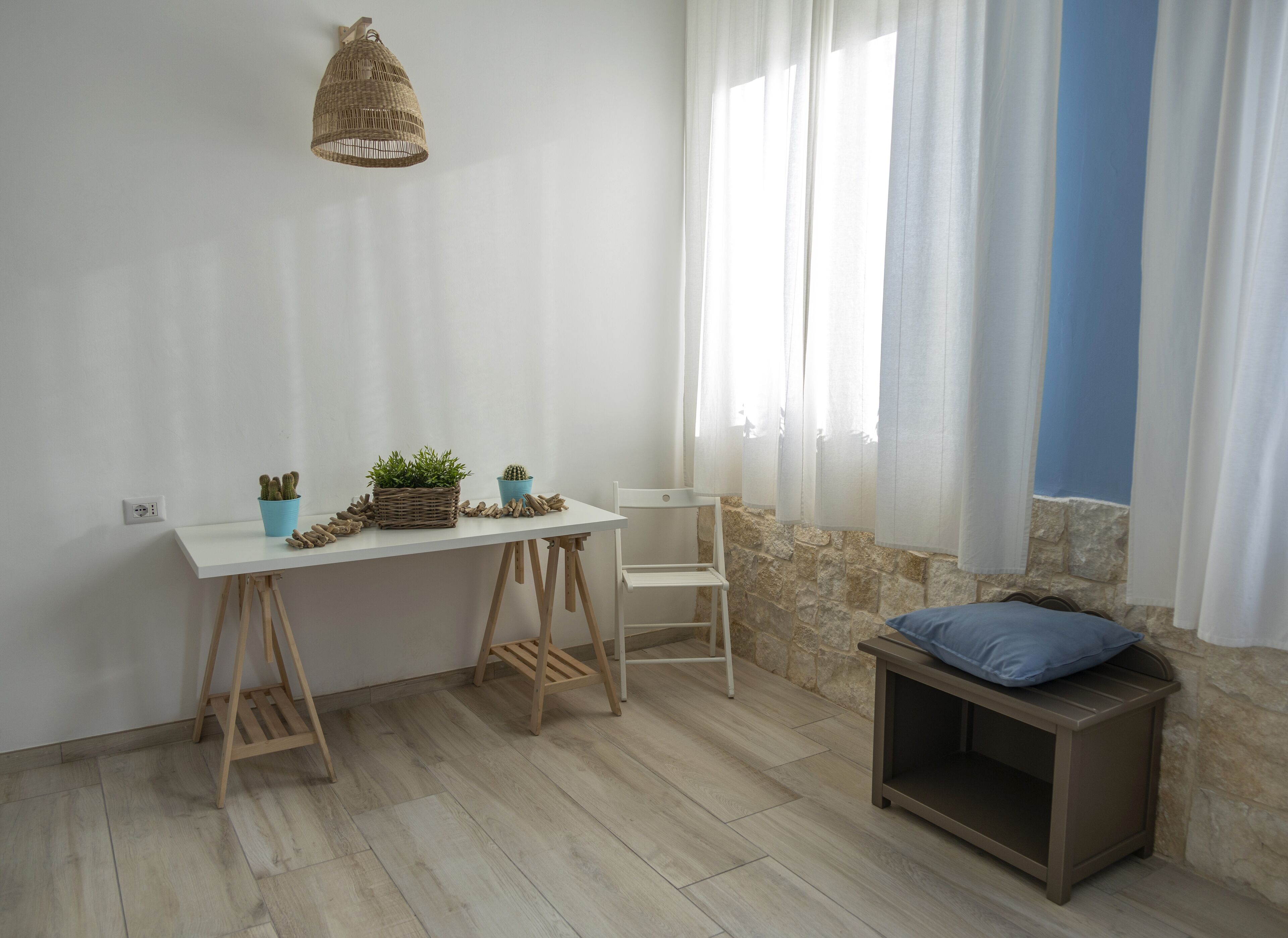 Una habitación con una mesa blanca, dos sillas, un pequeño banco, una lámpara colgante y una ventana con cortinas.
