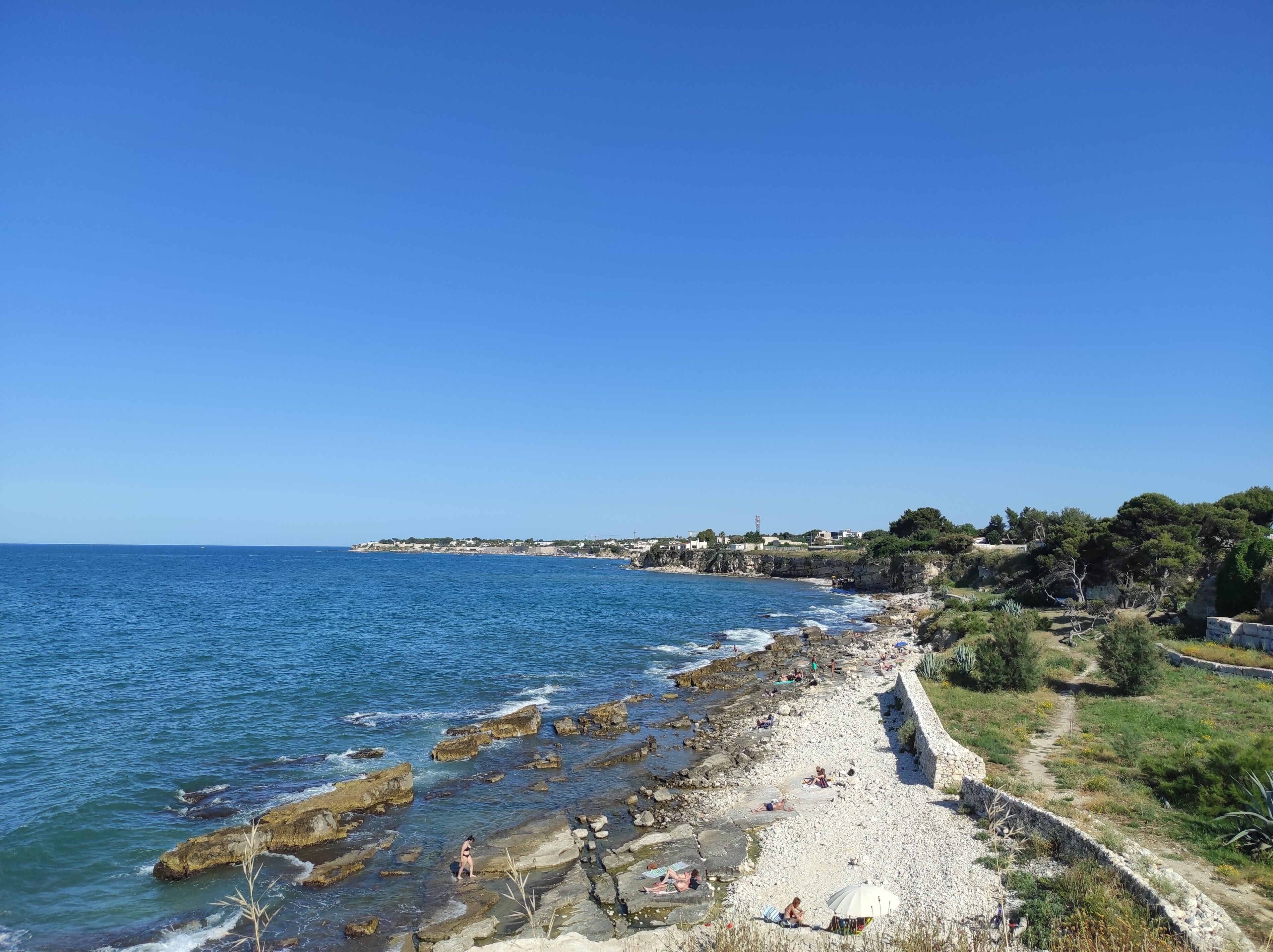 A coastal beach with rocky shores, a clear sky, and a distant town.