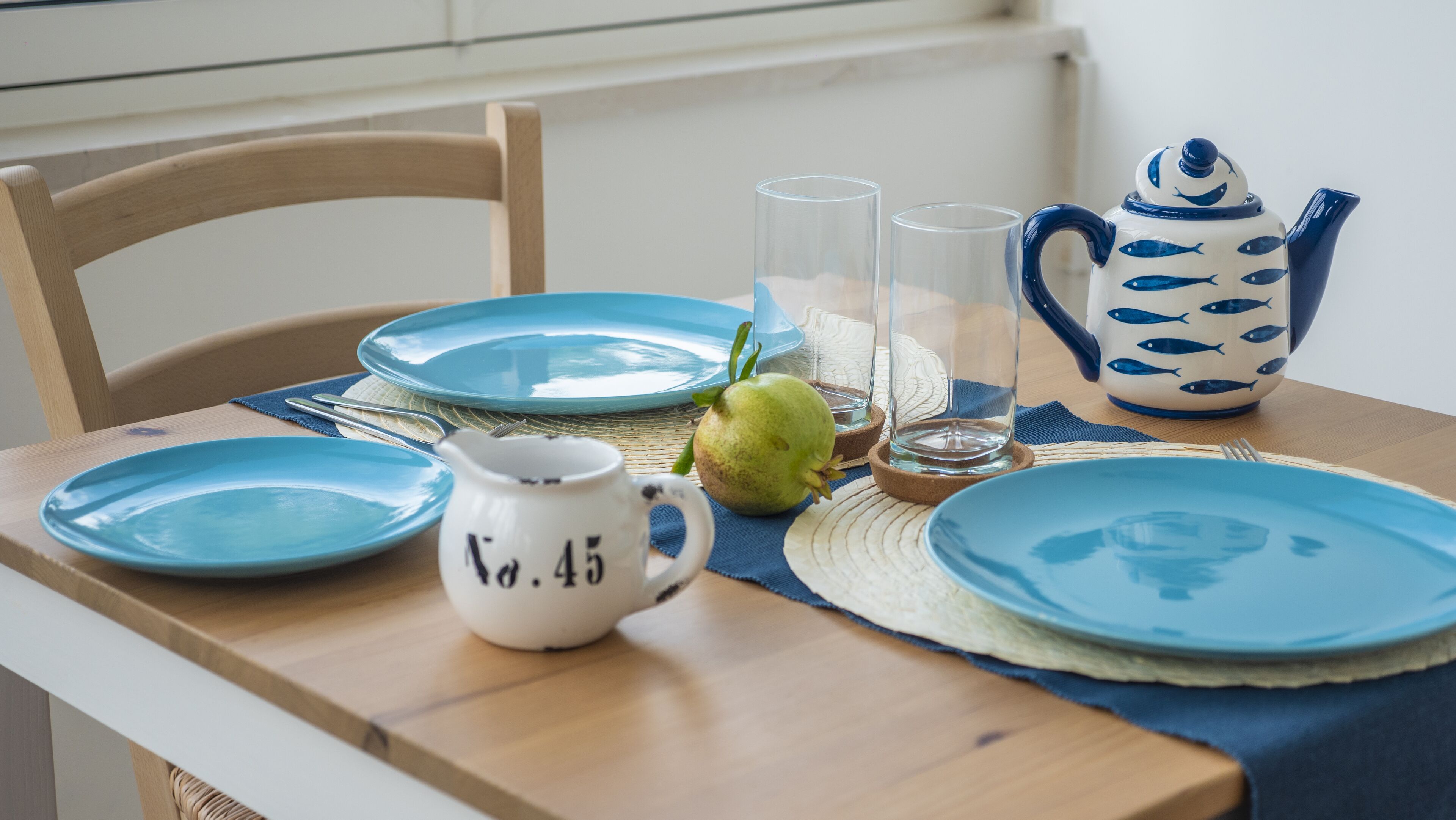 Une table dressée avec des assiettes bleues, un pichet blanc, un pichet en verre, un verre et une théière décorée de motifs de poissons.