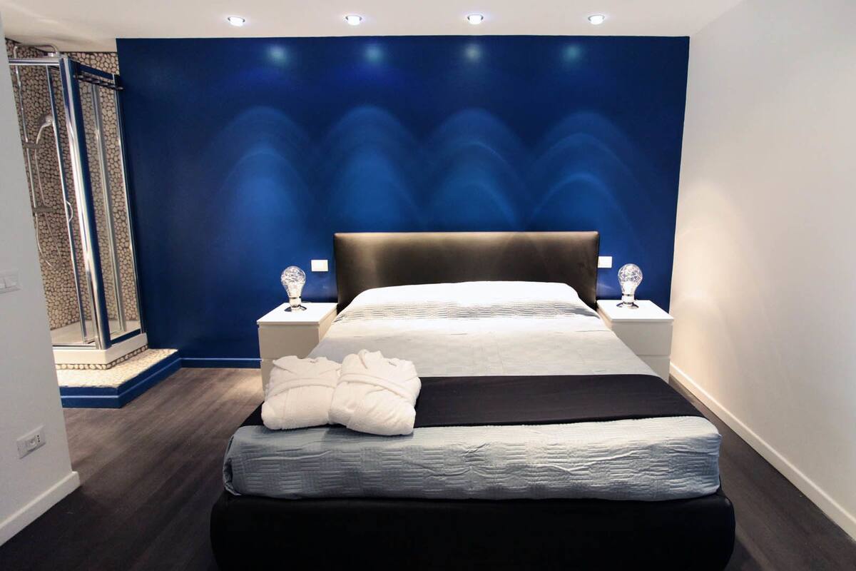 A modern bedroom with a large bed, a shower area, and a blue accent wall.
