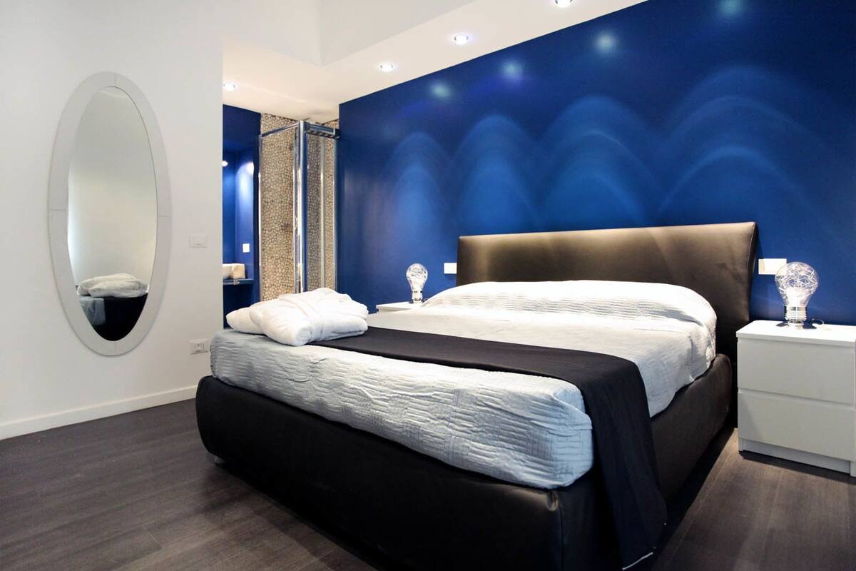 A modern bedroom with a large bed, a bedside table, a nightstand, a mirror, and a shower area.