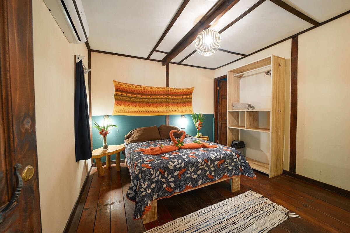 Une chambre à coucher comprenant un lit, une armoire en bois, une tapisserie murale, une petite table avec une lampe et une plante décorative.