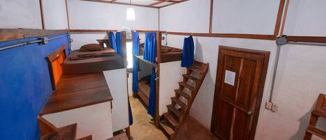 Ein kleines Zimmer mit Etagenbetten, einer Holzleiter, einer Tür und einem kleinen Fenster.