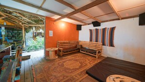 A rustic room with a wooden bench, a small table, a patterned rug, and a wall with a striped textile. - Playa 506 Beachfront Hostel (Cahuita)