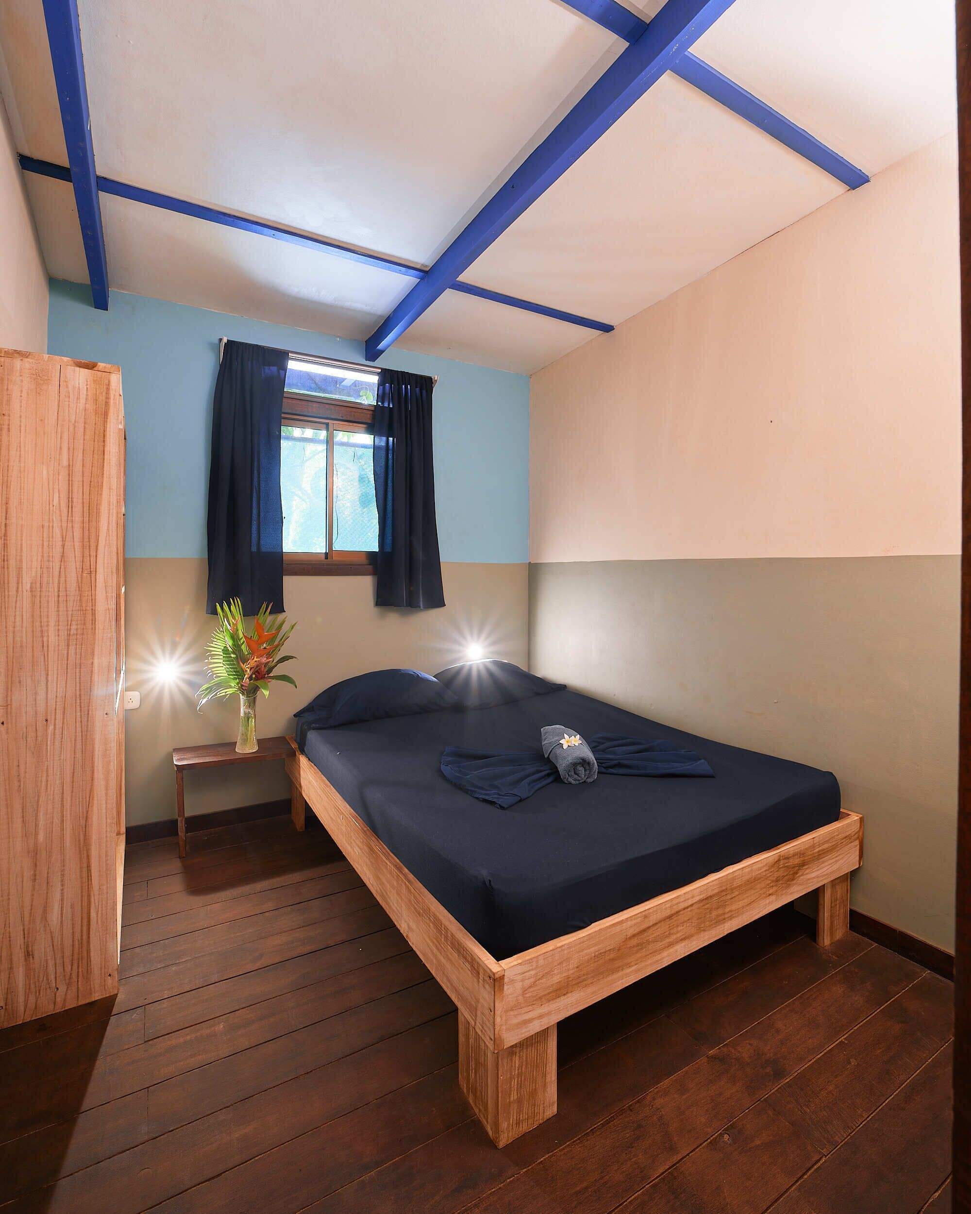 A single bed with a wooden frame, a small bedside table with a vase, and a window with curtains.