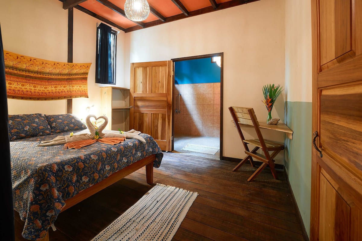 Une chambre à coucher comprenant un lit, une armoire en bois, une chaise, une petite table et un luminaire suspendu.