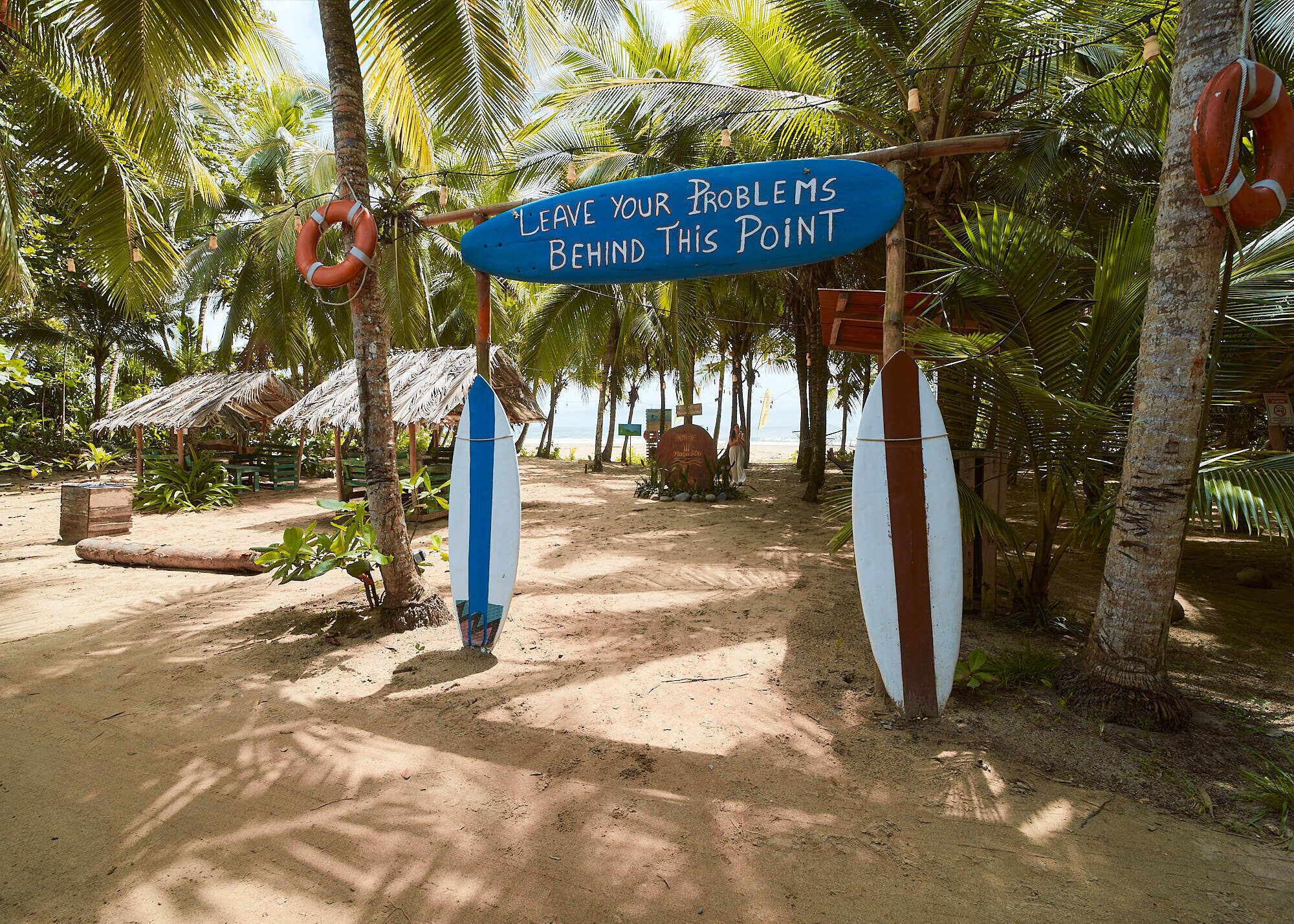 A beach with surfboards and a sign that reads "Leave your problems behind this point."