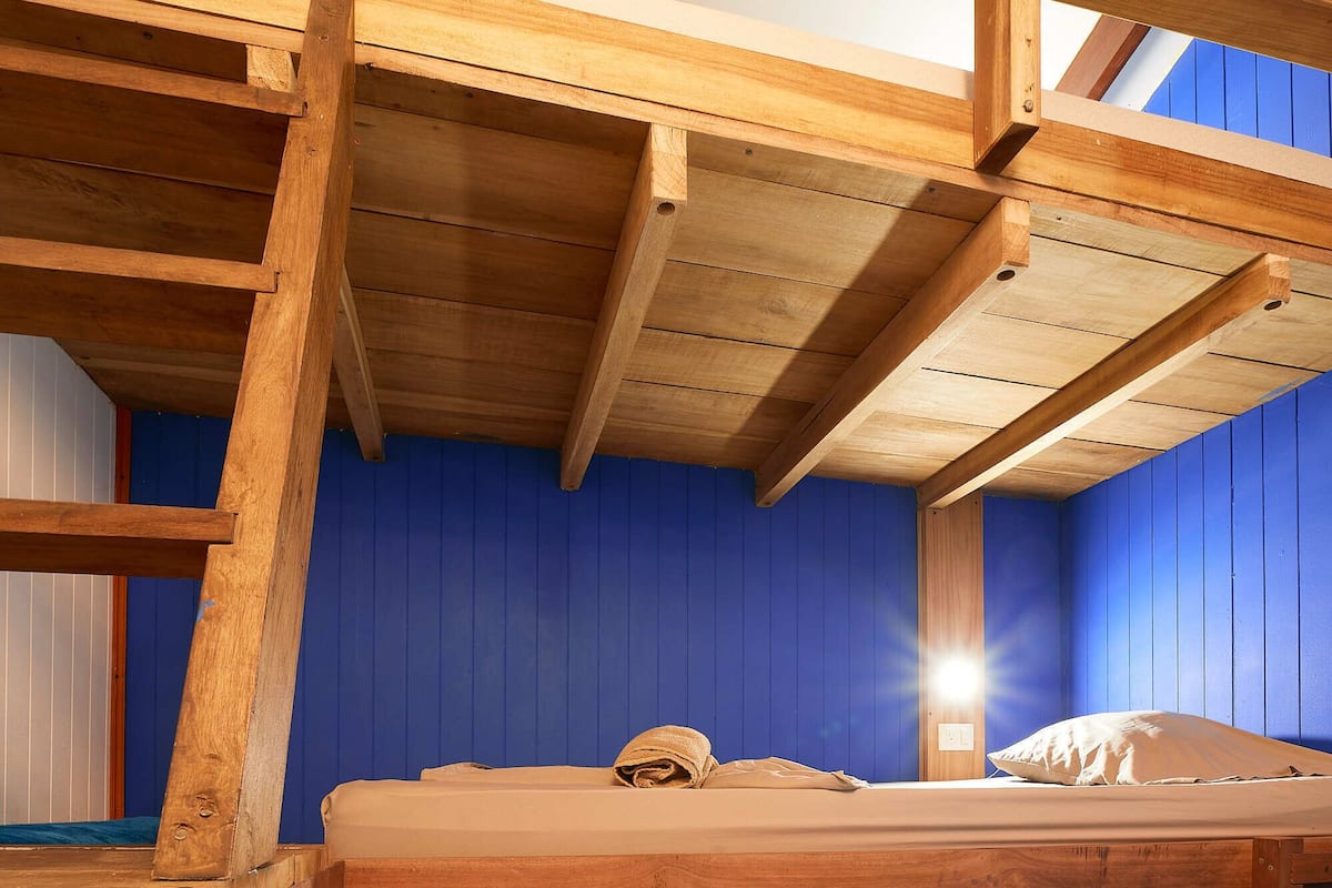Un lit superposé avec un mur bleu et des poutres en bois au plafond.