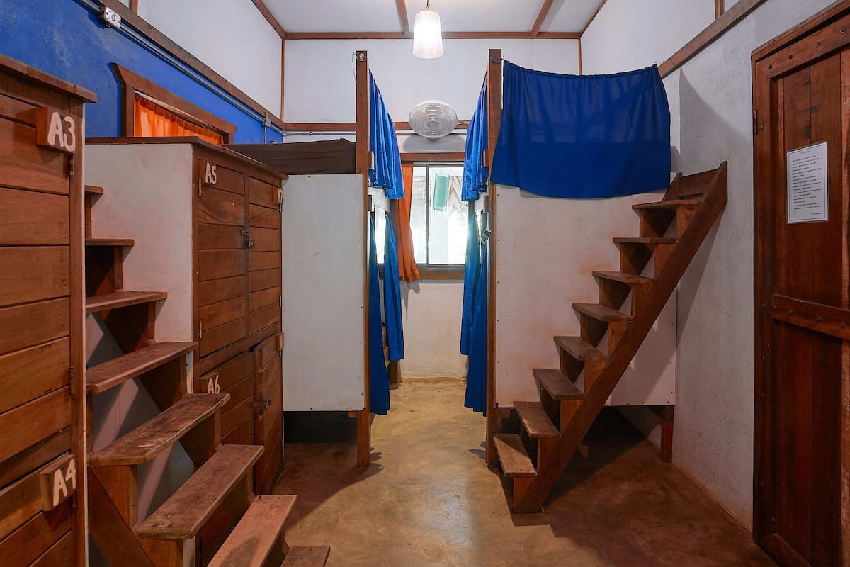 Un couloir avec des lits superposés en bois, un escalier et un ventilateur.