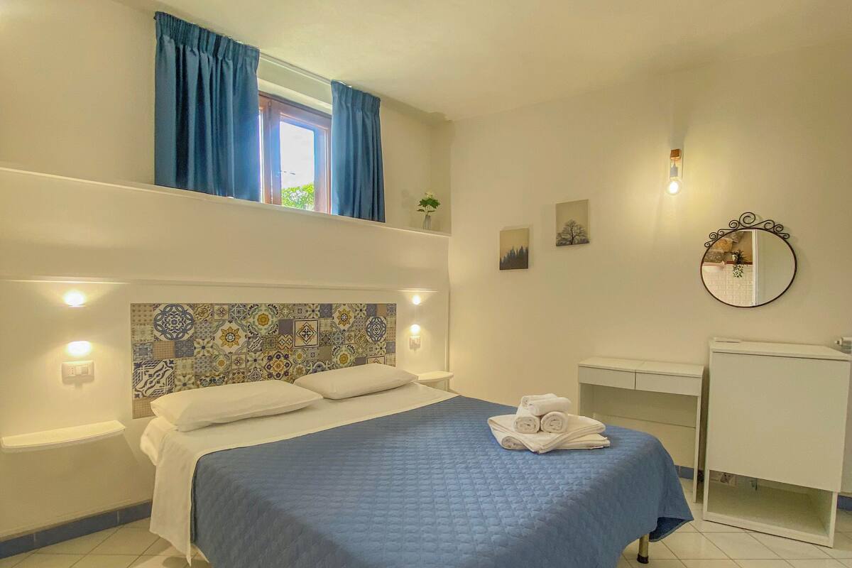 A bedroom with a bed, a desk, and a mirror.