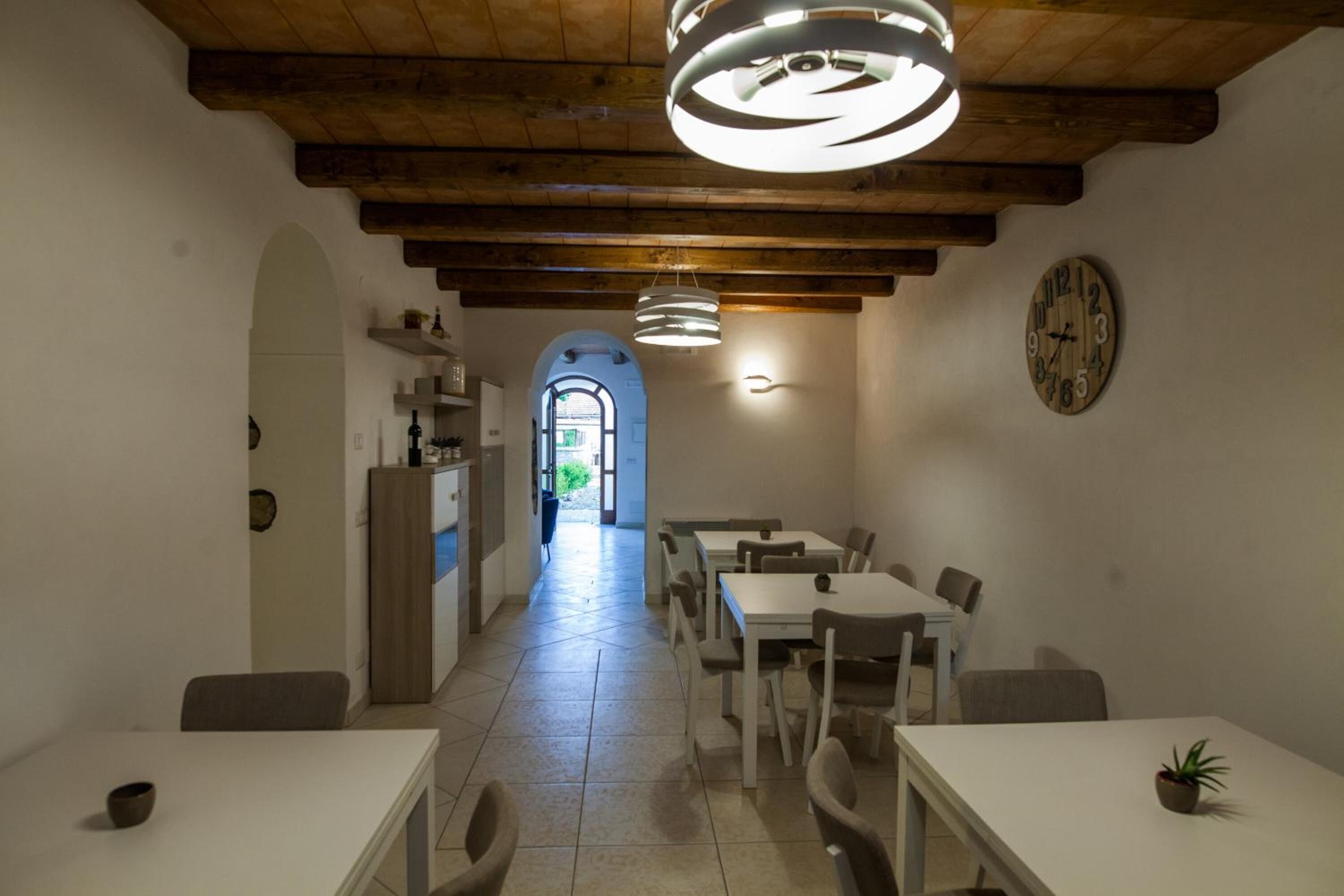 A dining area with white tables and chairs, a wooden ceiling, and a clock on the wall.