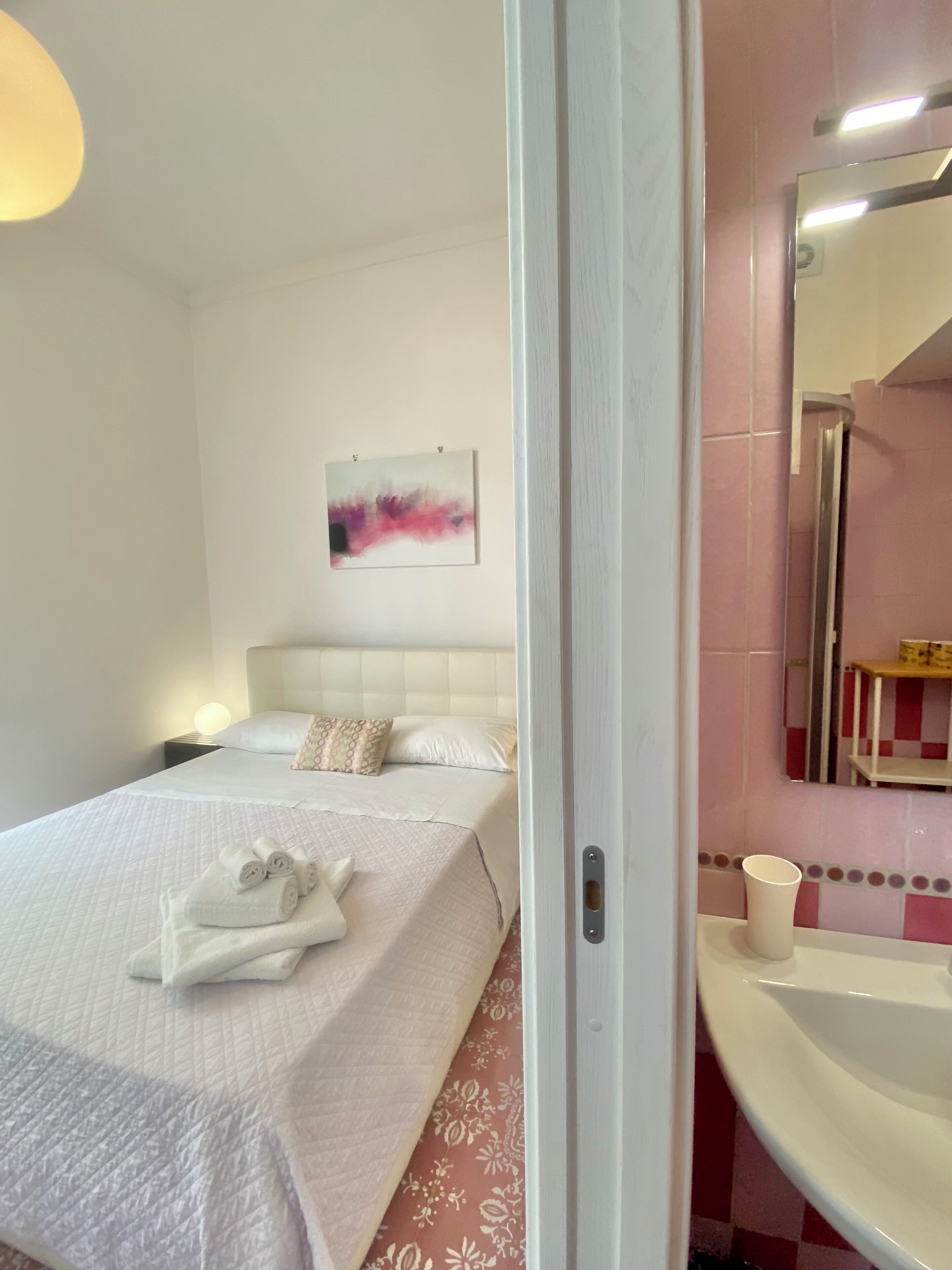 A hotel room with a bed, a bedside table, a wall-mounted painting, a bathroom with a sink and mirror.