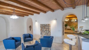 Un interno moderno con poltrone blu, una parete a contrasto in pietra e un angolo cottura con sgabelli da bar.