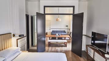 A hotel room with a bed, a desk, a chair, a television, and a view into the dining area.