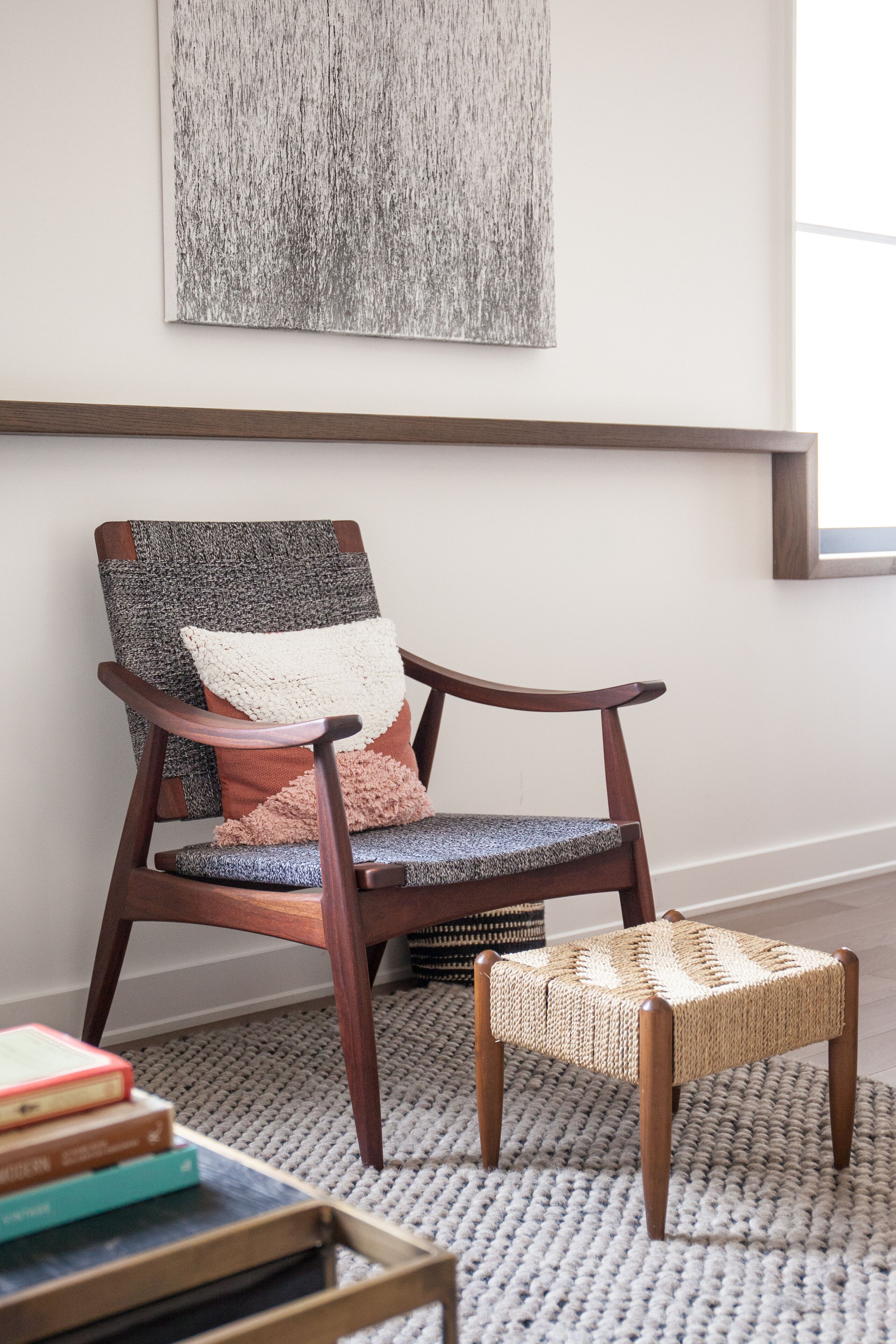 A wooden chair with a woven seat and backrest, a small stool, and a framed artwork on the wall.