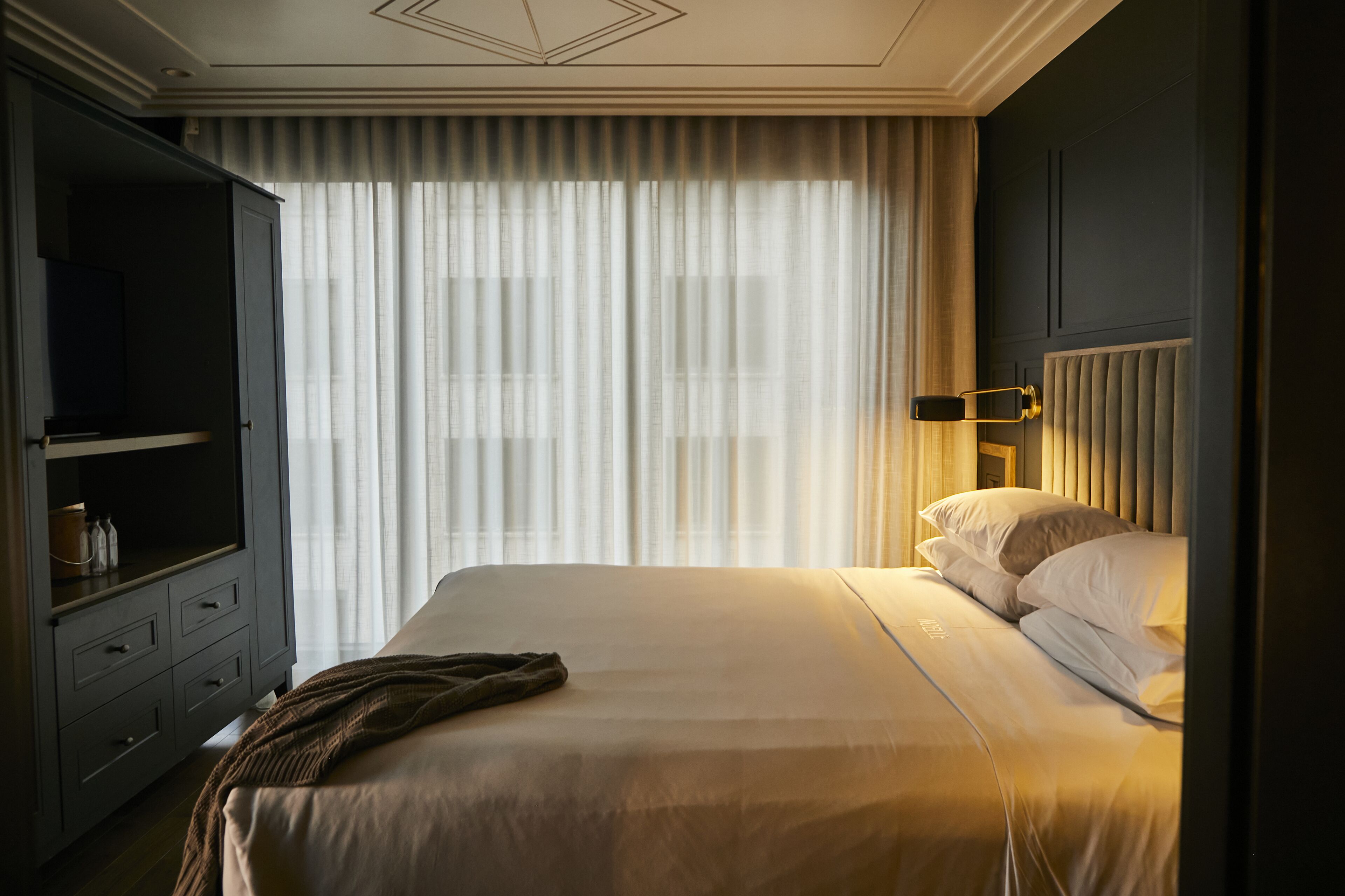 A hotel room with a bed, a television on a cabinet, and a window with curtains.