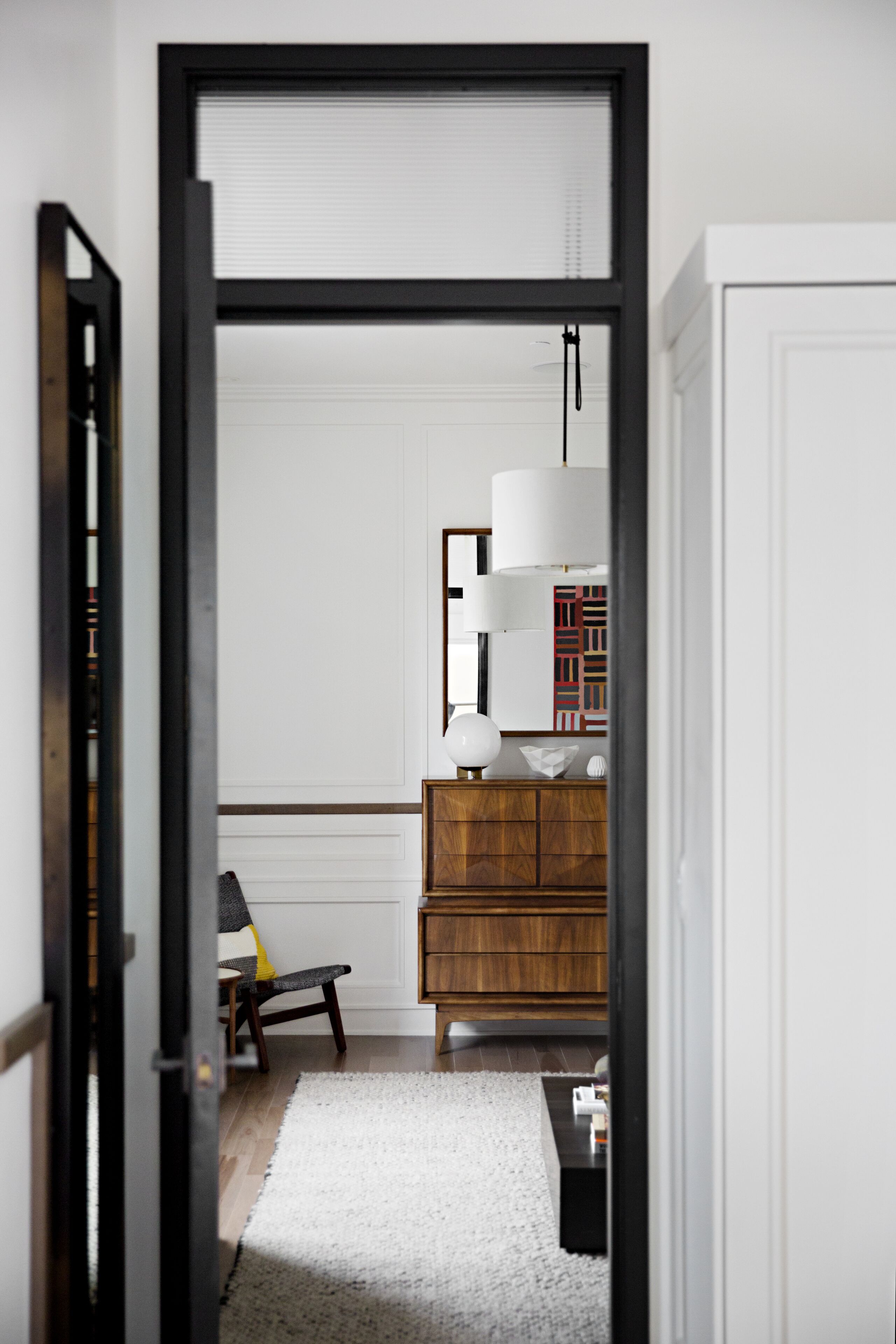 A hallway with a wooden floor, a white rug, a wooden cabinet, and a chair.