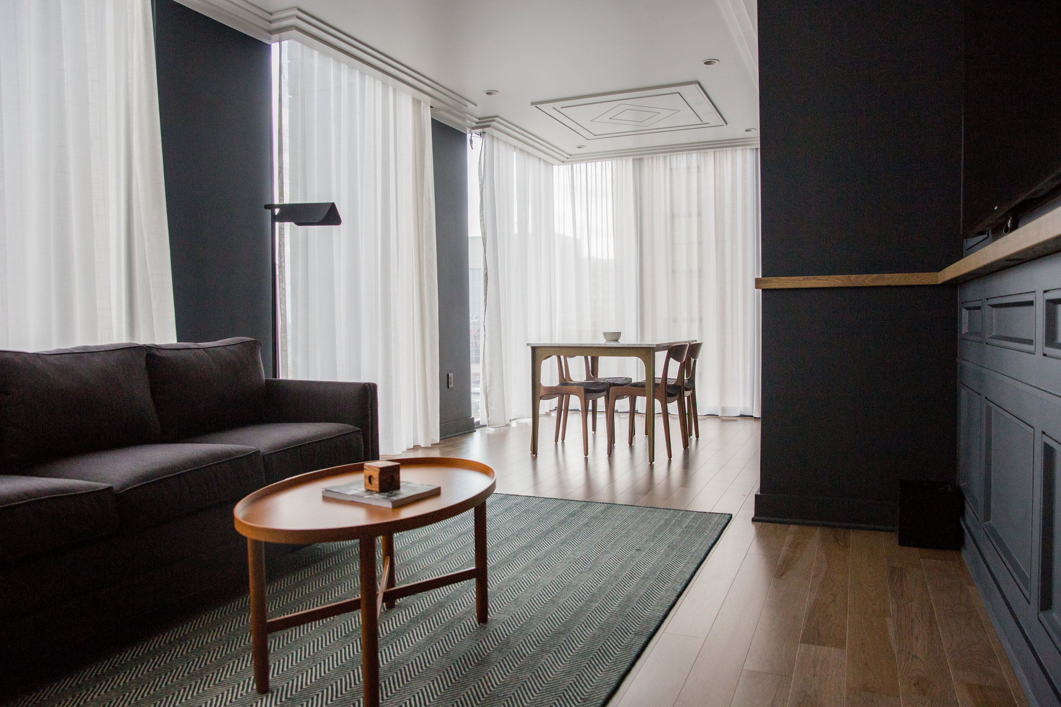 Een moderne woonkamer met een donkergrijze bank, een houten salontafel en een eethoek met een tafel en stoelen.