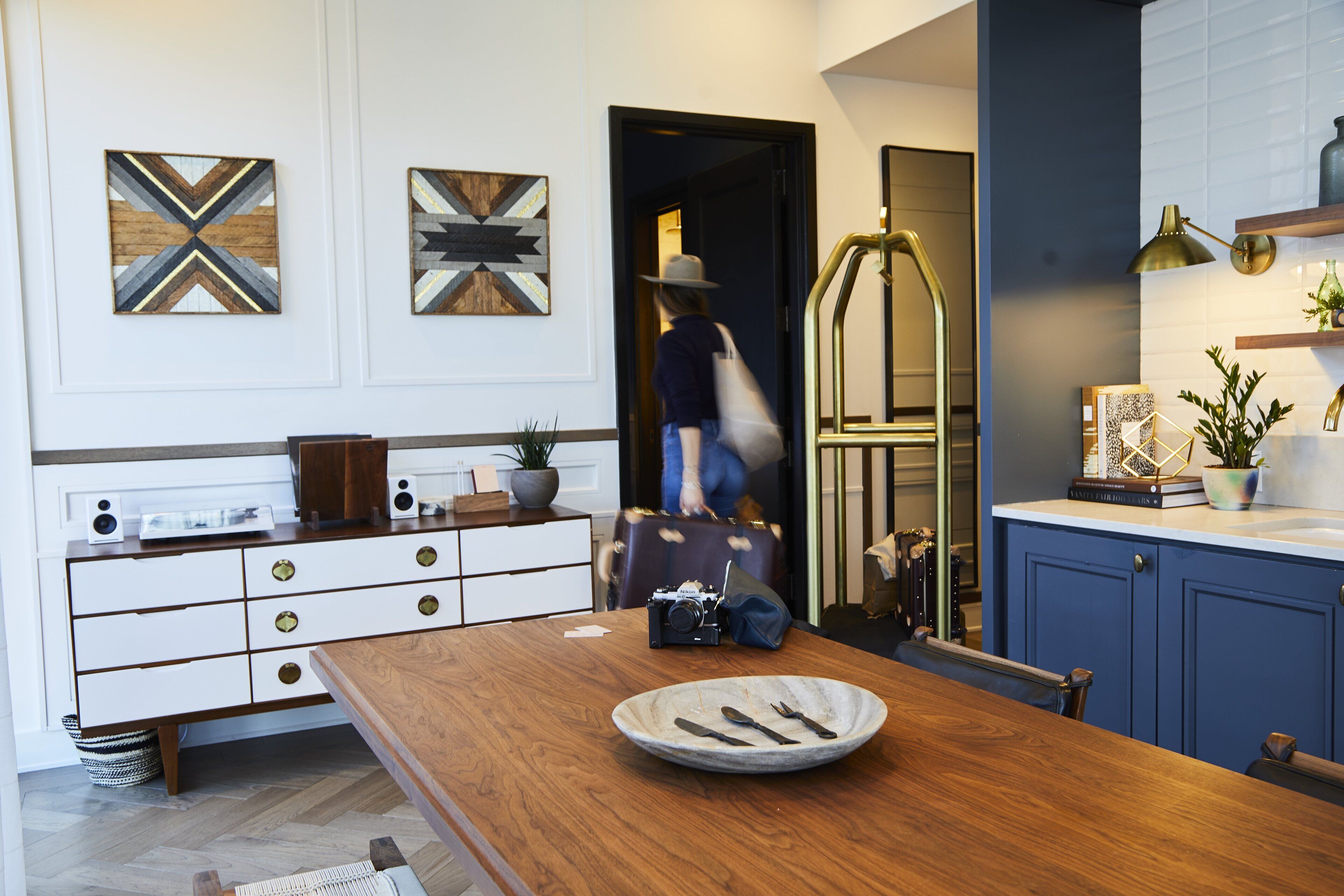 A modern kitchen with a wooden dining table, a bowl of cutlery, and a camera on the counter.