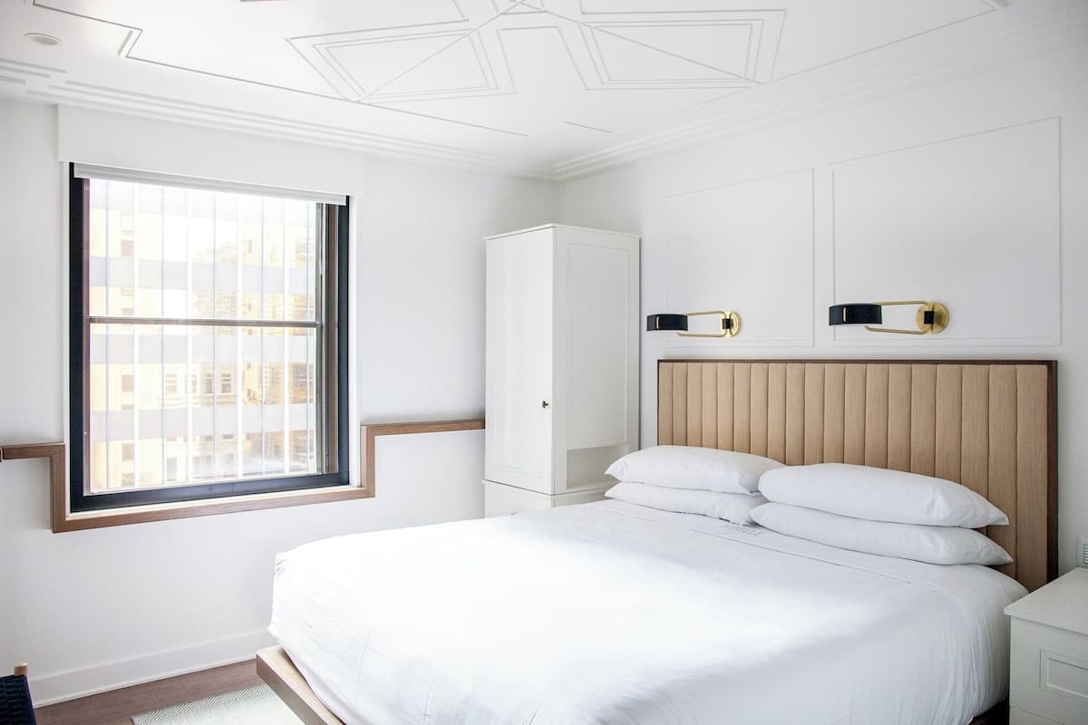 A bedroom with a large bed, a wardrobe, and a window with blinds.