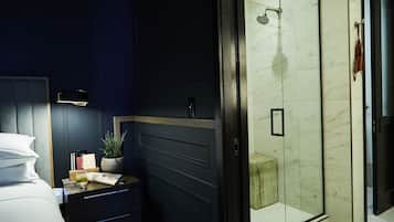Una habitación de hotel moderna con cama, mesita de noche y zona de ducha con cerramiento de vidrio.