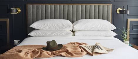 A neatly made bed with white linens, a brown throw blanket, a hat, and a newspaper.
