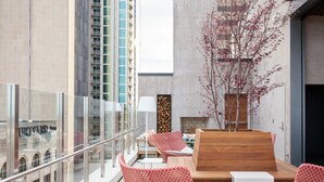 Un área de estar moderna al aire libre con sillas de diseño rojo con estampado y un banco de madera, con vista a un paisaje urbano de edificios altos.