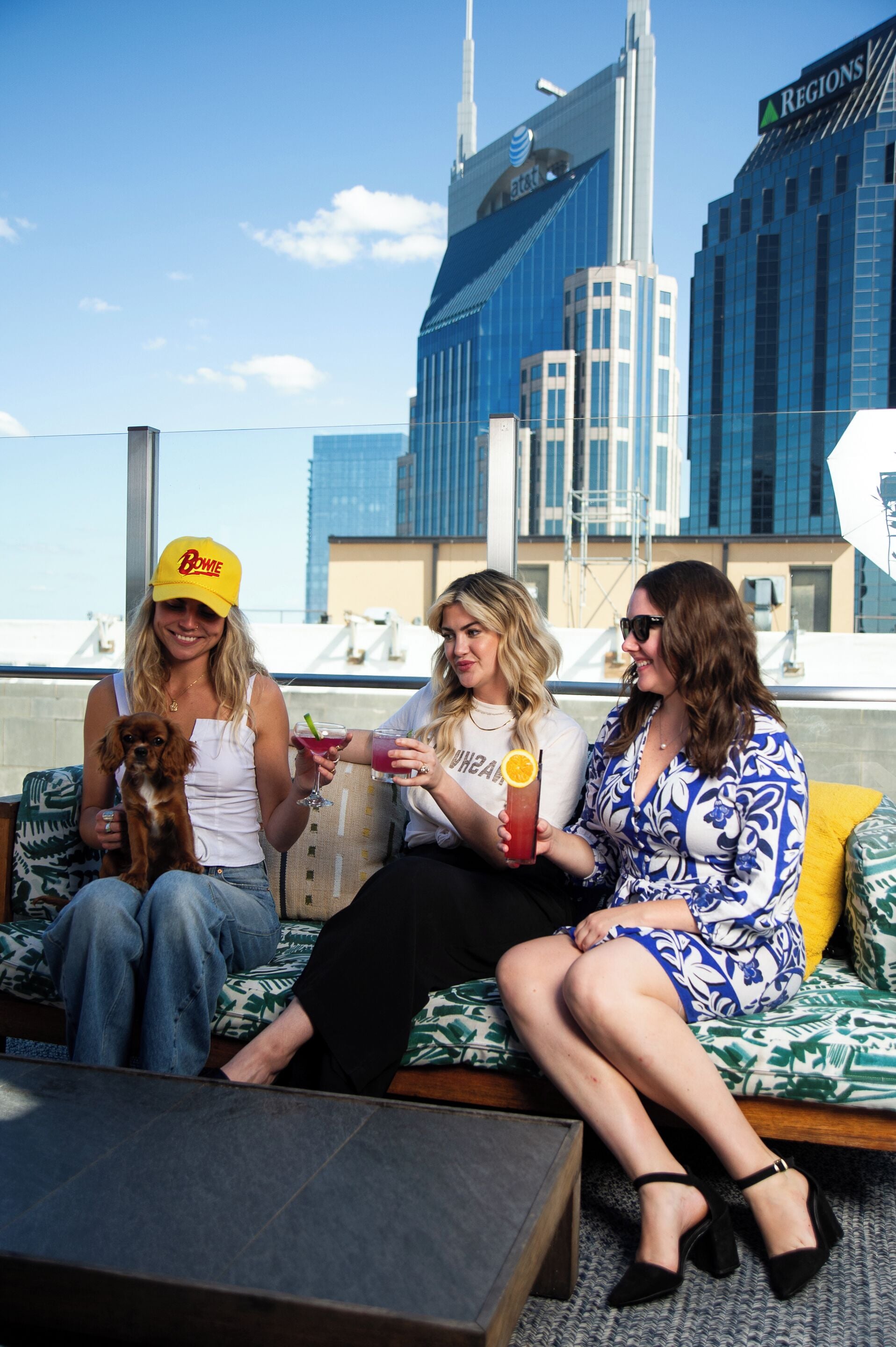 Three people sitting on a balcony with a city skyline in the background.