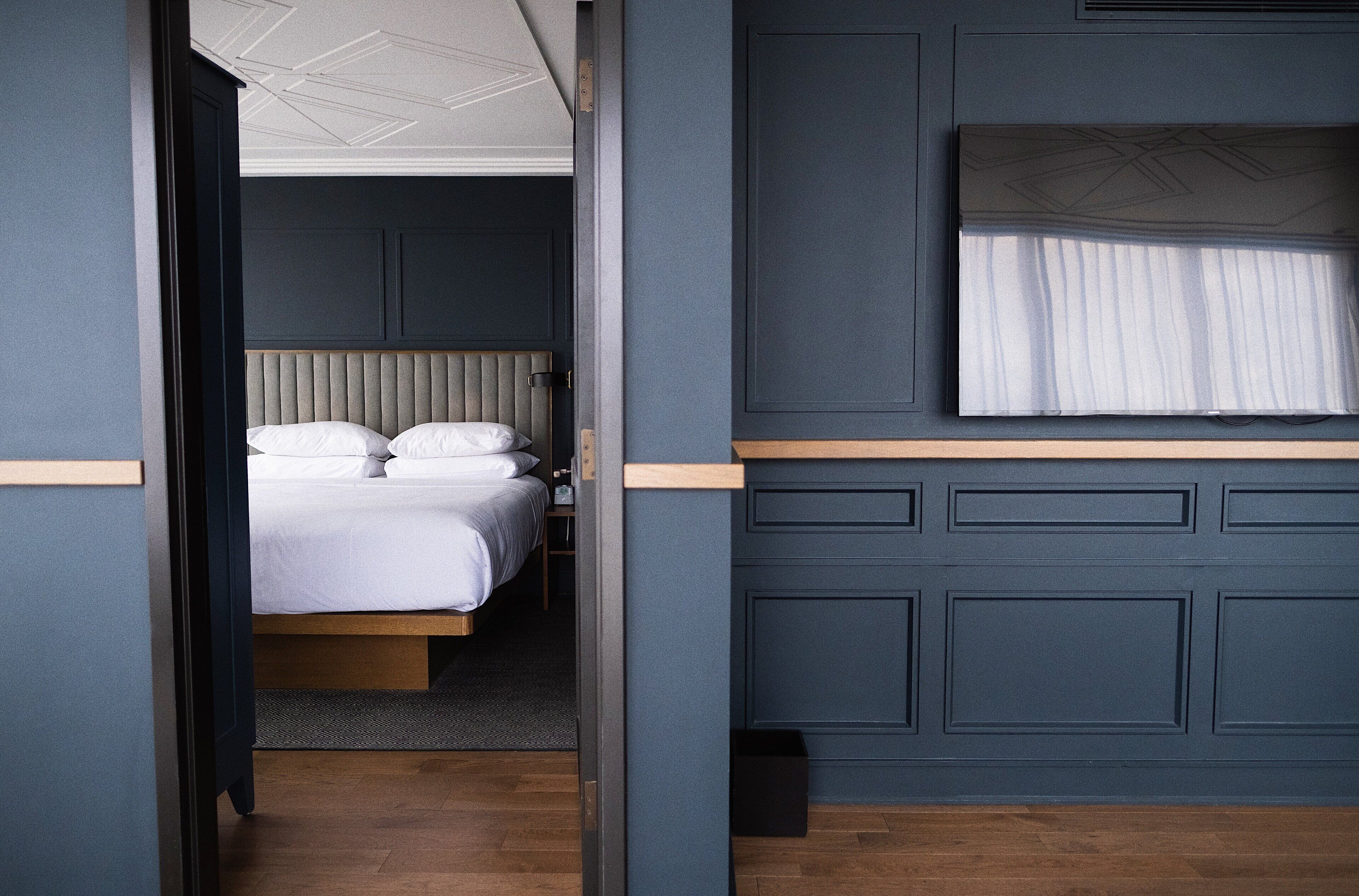 A hotel room with a bed, a window with curtains, and a wooden floor.