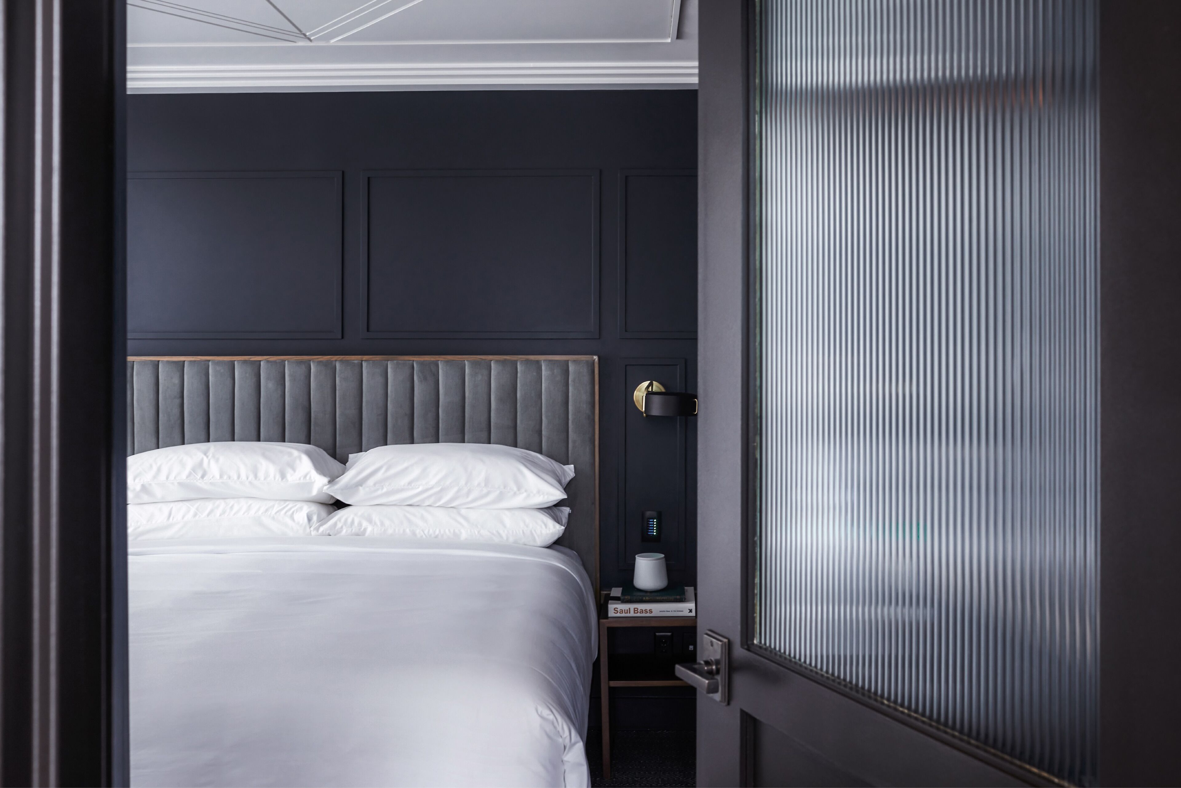 Una habitación de hotel moderna con una cama grande, una mesita de noche y una lámpara fijada a la pared.