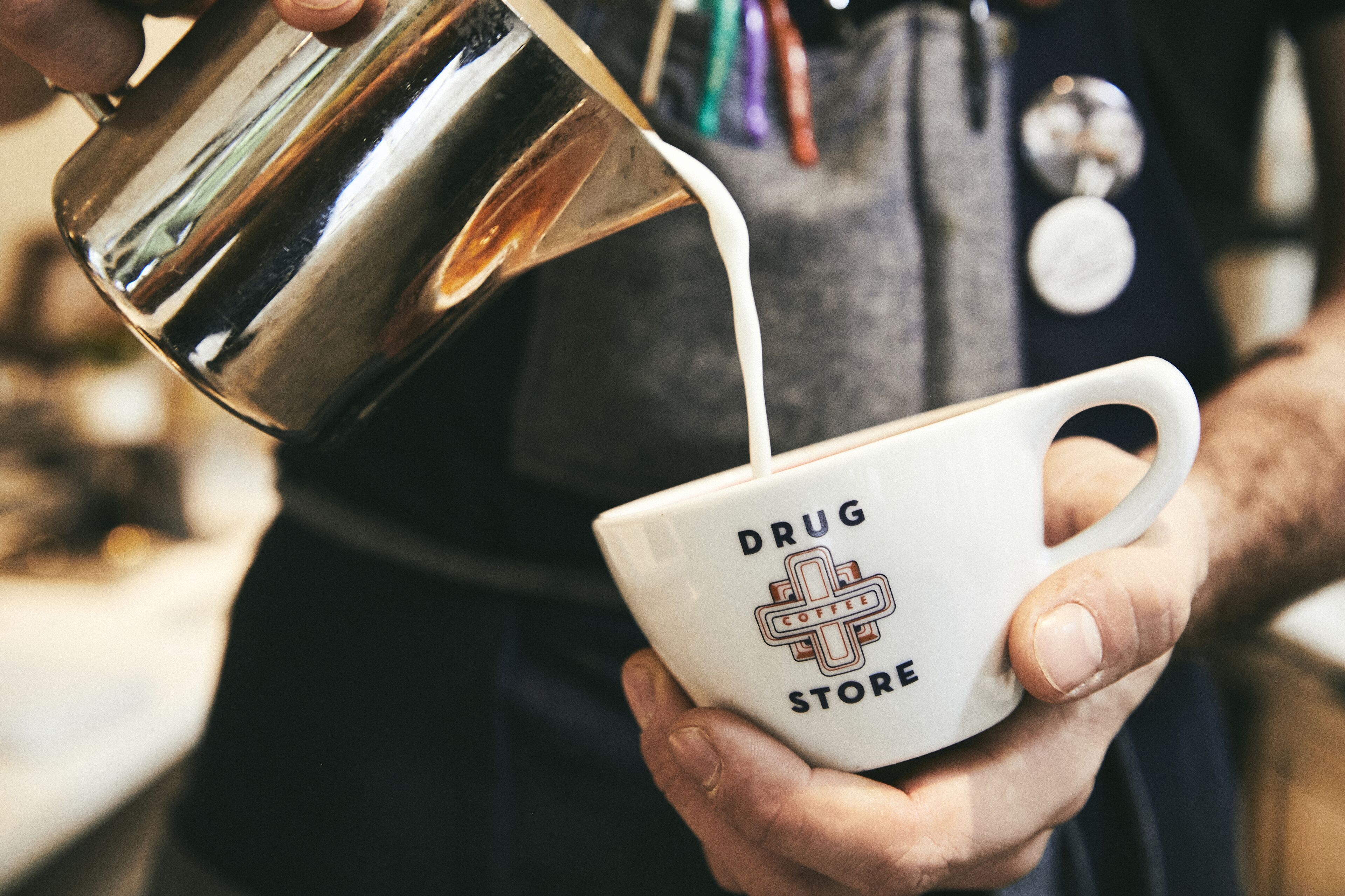 A person pouring milk into a mug with a logo that reads "DRUG STORE."