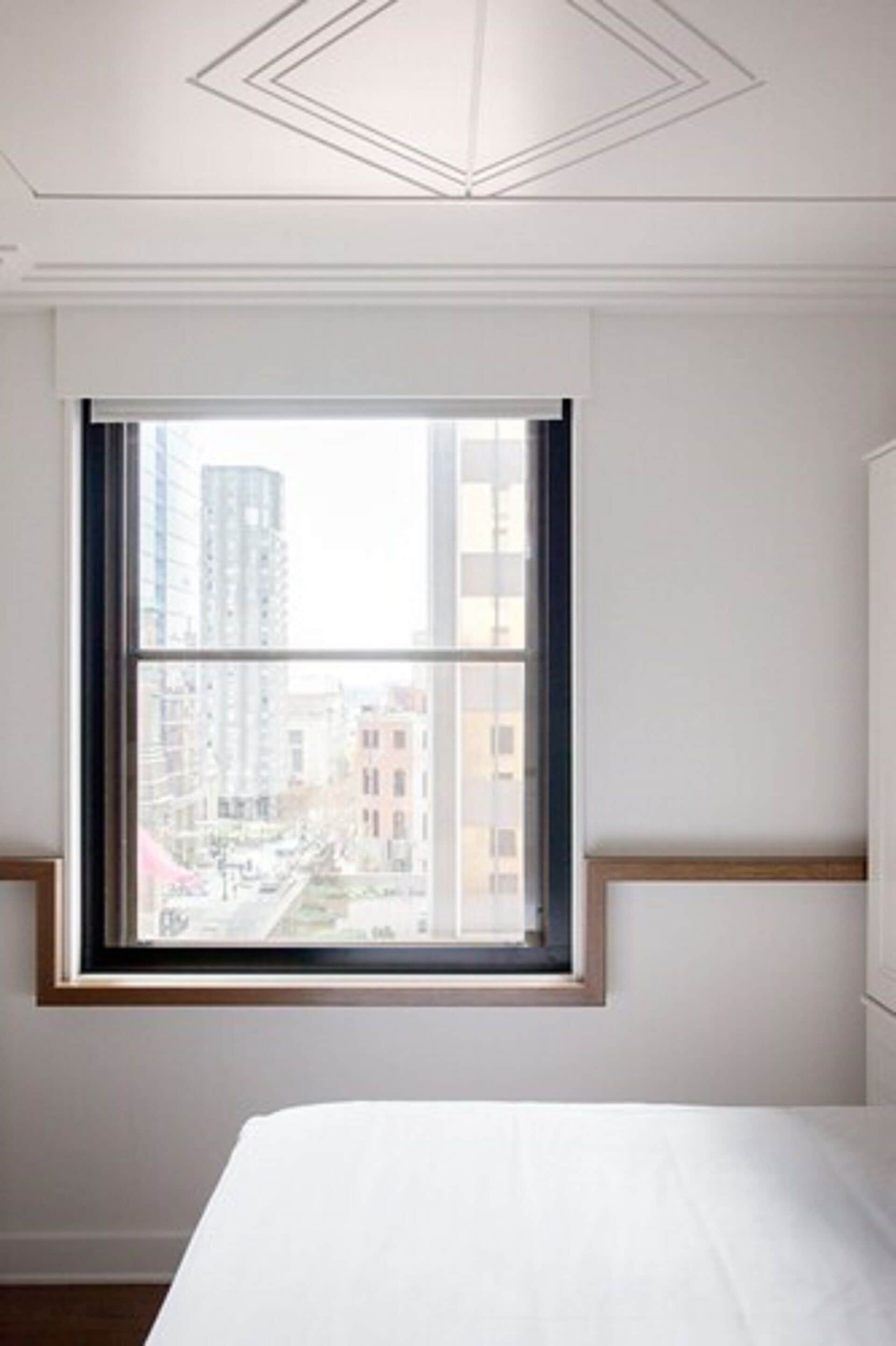 Une chambre avec une grande fenêtre, un lit et une vue sur les bâtiments environnants.