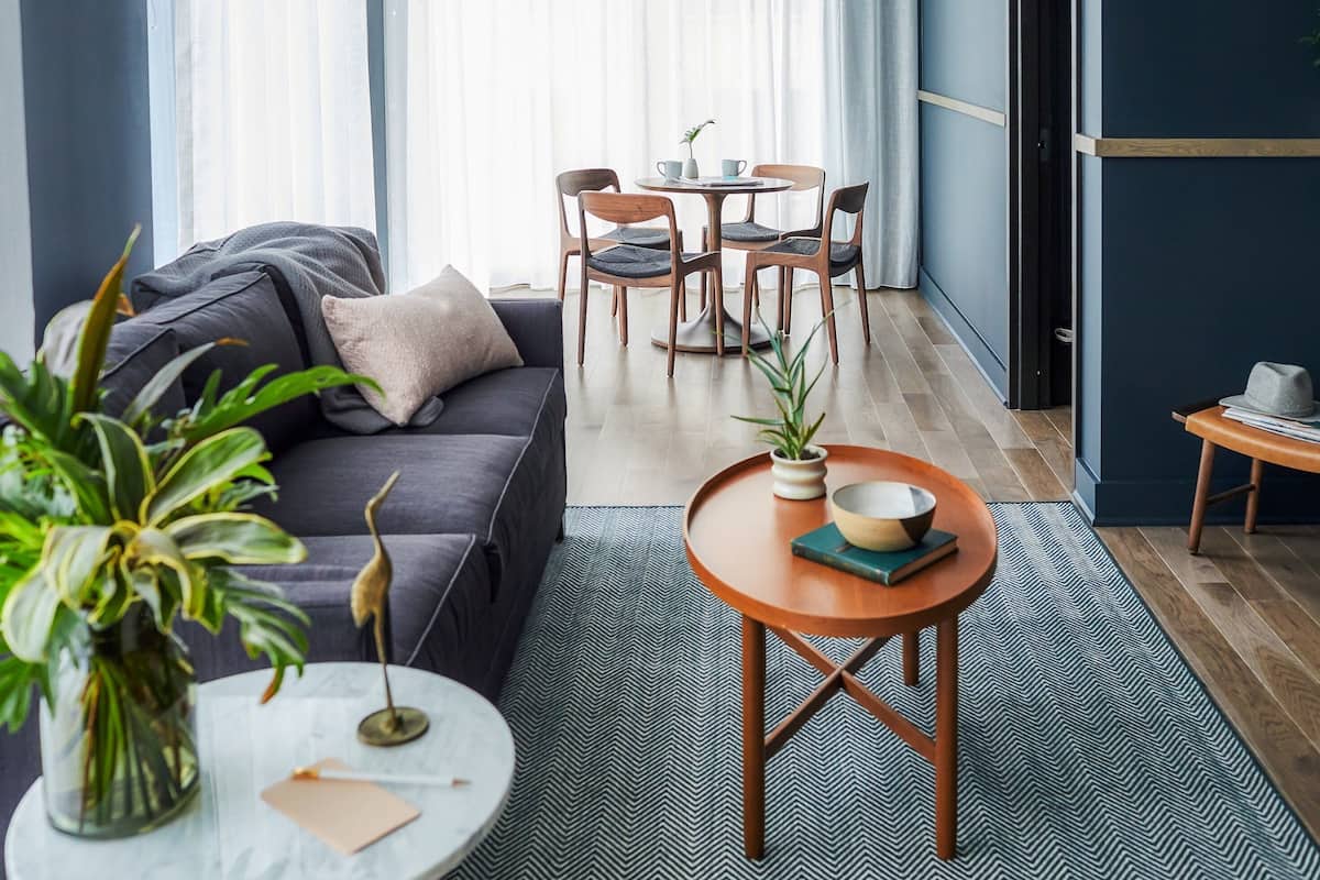 A modern living room with a sofa, a round wooden table, and a dining area with chairs.