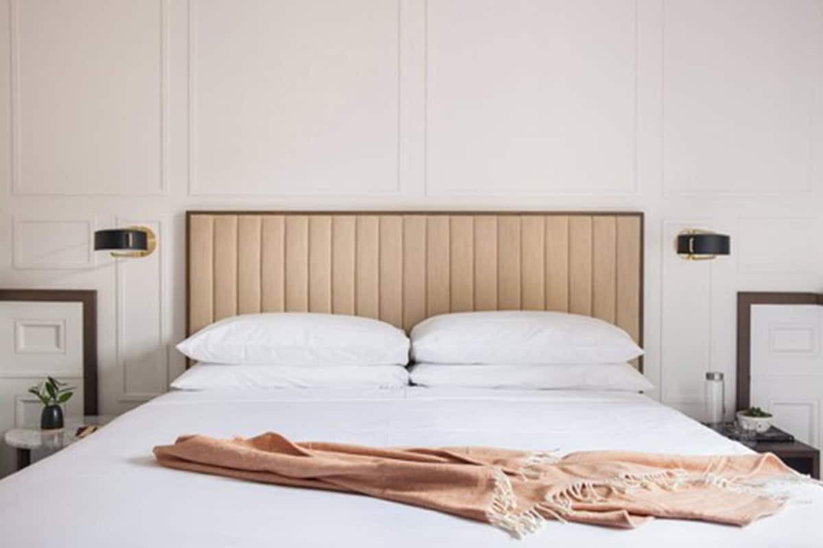A neatly made bed with white linens and a beige throw blanket, flanked by bedside tables with lamps.